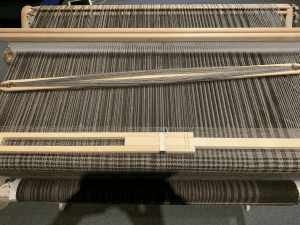 A loom with a work in progress, warp threads in chocolate and silver running from top of image to bottom.