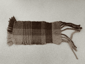 A small hand woven sample in chocolate brown and silver grey, showing different weave structures, fringe finishes and colour combinations.